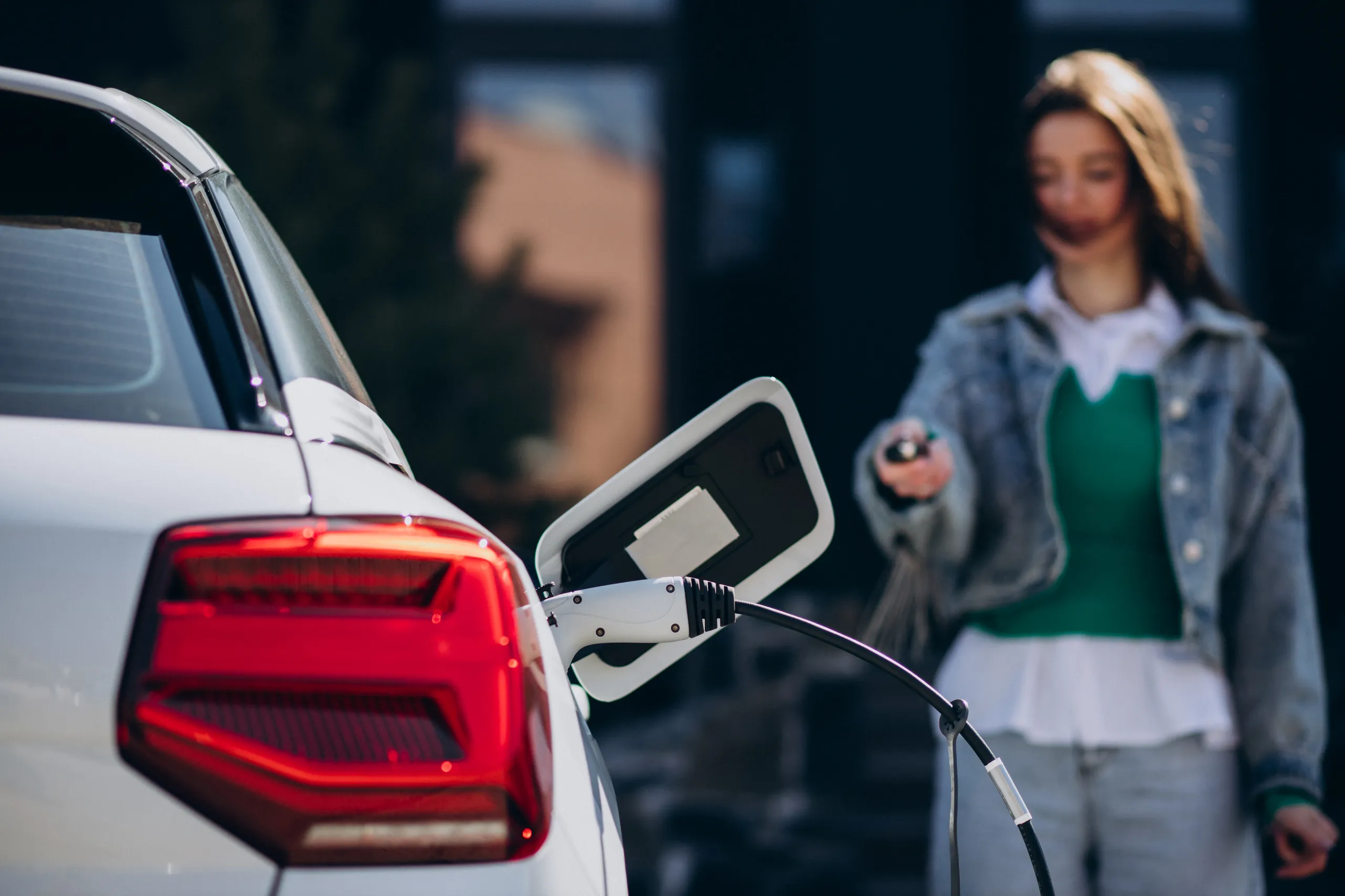 Coche eléctrico blanco cargando mientras una persona sostiene el conector de carga