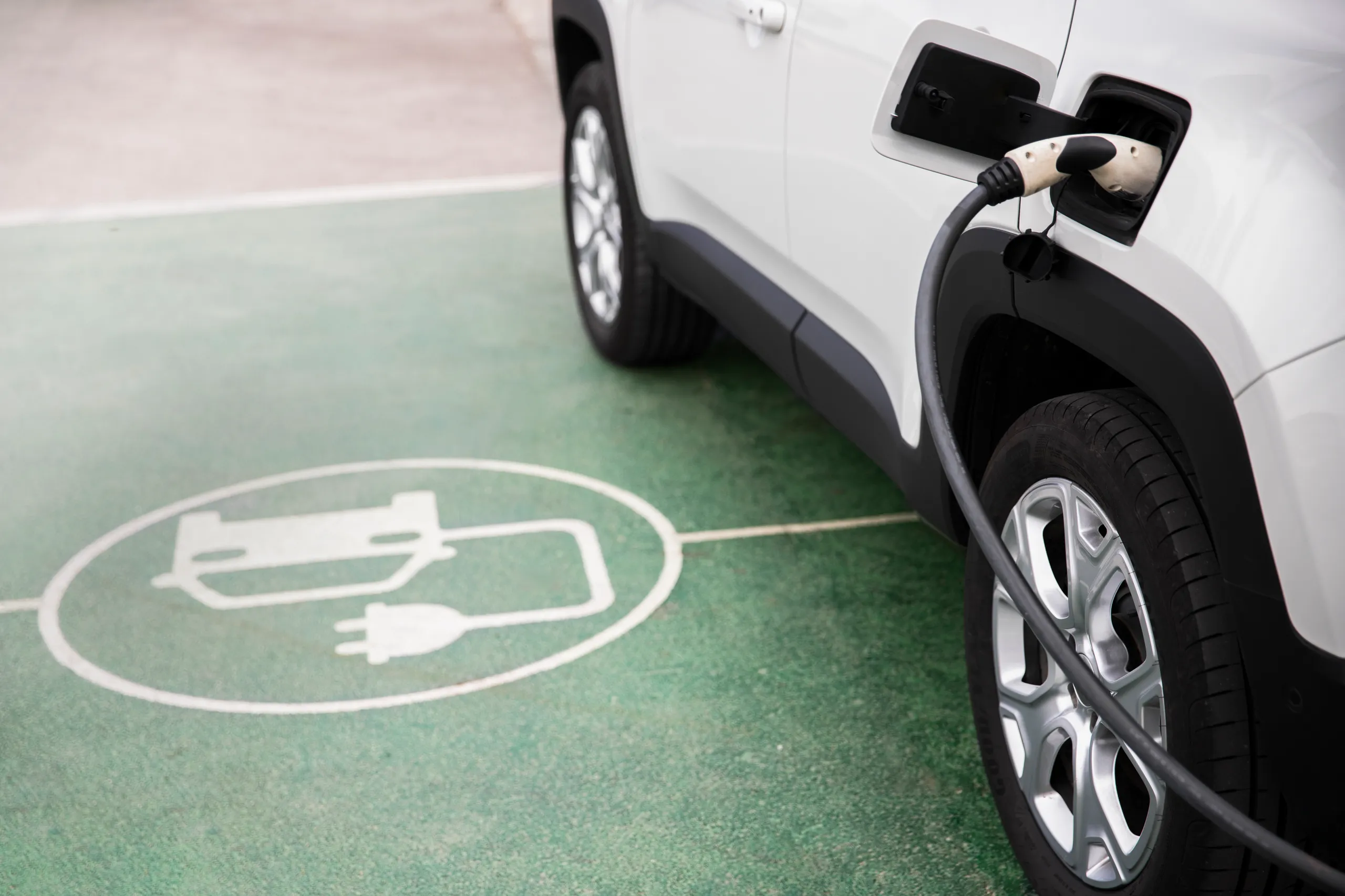 Coche eléctrico blanco enchufado en punto de carga con símbolo de batería en el suelo