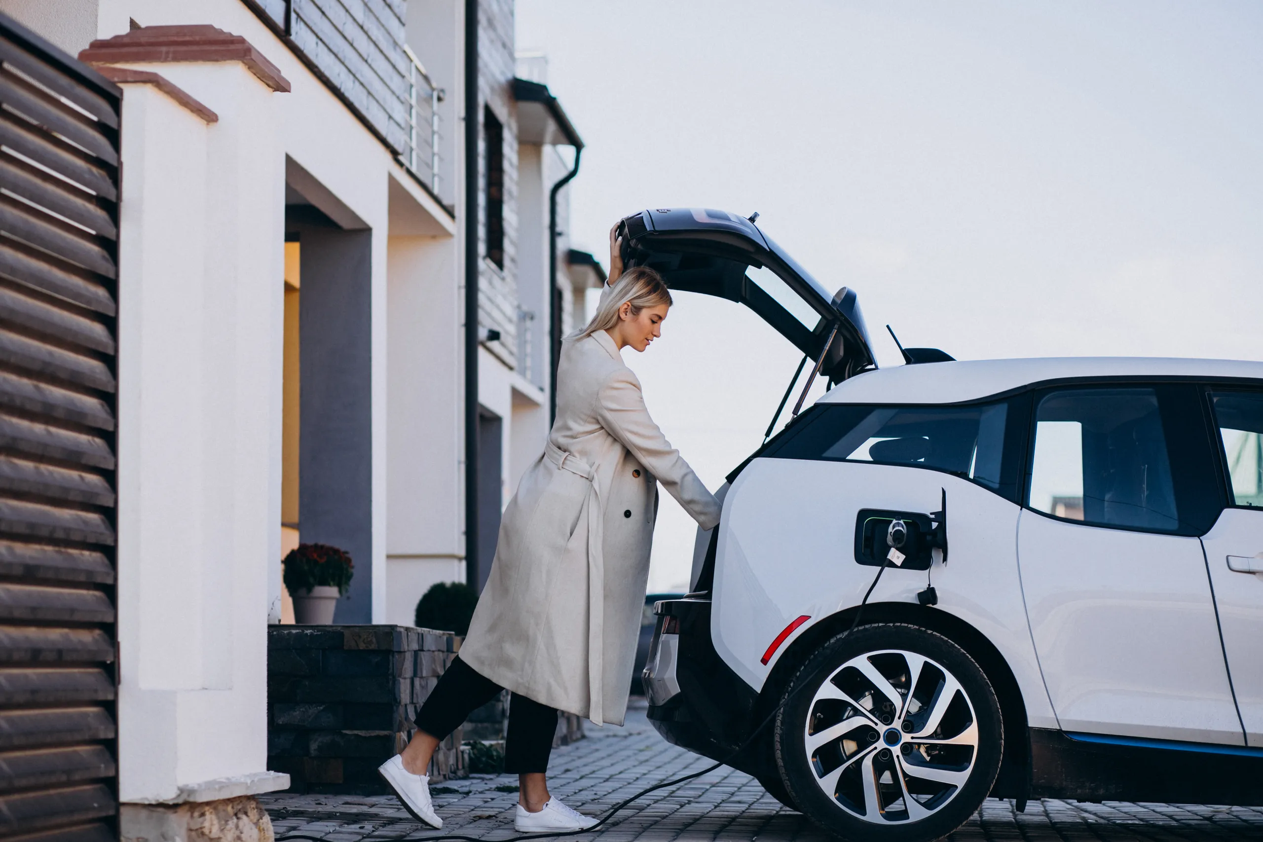 Mujer cargando coche eléctrico blanco en garaje de vivienda moderna