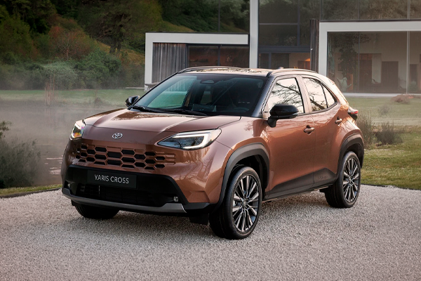 Toyota Yaris Cross cobre metalizado con llantas de aleación sobre grava, frente a una casa moderna con grandes cristaleras