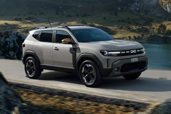 Dacia Duster gris arena con barras de techo en una carretera junto a un lago de montaña y laderas amarillentas