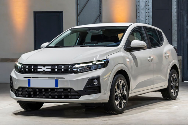 Dacia Sandero blanco perla con parrilla negra y llantas de aleación, aparcado en una nave de paredes grises con focos cálidos