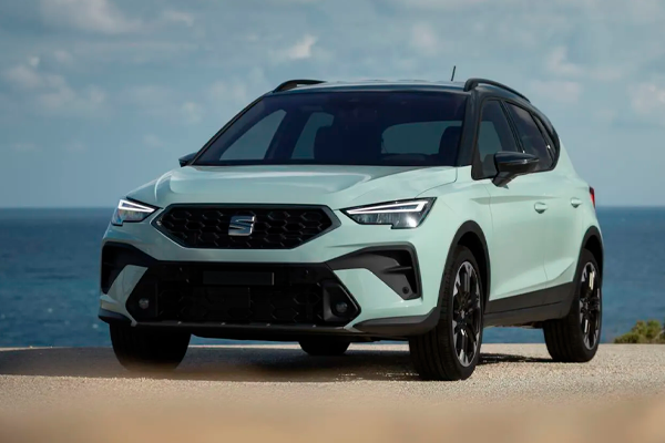 SEAT Arona verde menta con parachoques y pasos de rueda negros, parado frente al mar bajo un cielo con nubes