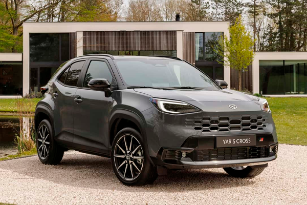 Toyota Yaris Cross gris oscuro con llantas de aleación sobre un camino de grava, delante de una casa moderna con cristaleras