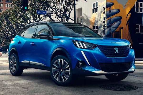Peugeot 2008 azul con techo negro parado en una calle de ciudad, junto a un edificio con un mural pintado de colores