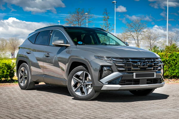 Hyundai Tucson gris con llantas de aleación y luces diurnas en la parrilla, aparcado sobre adoquines junto a un seto