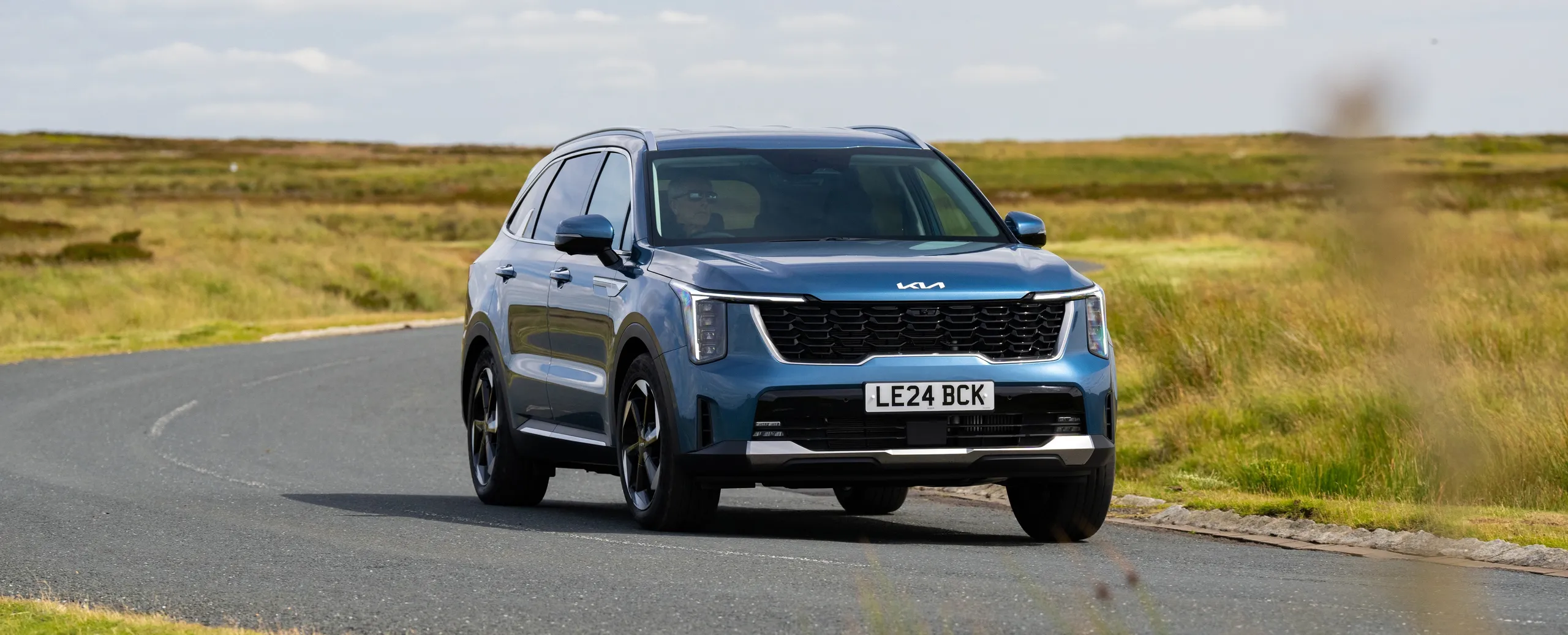 Kia Niro azul de 7 plazas circulando por carretera rural con paisaje de campo