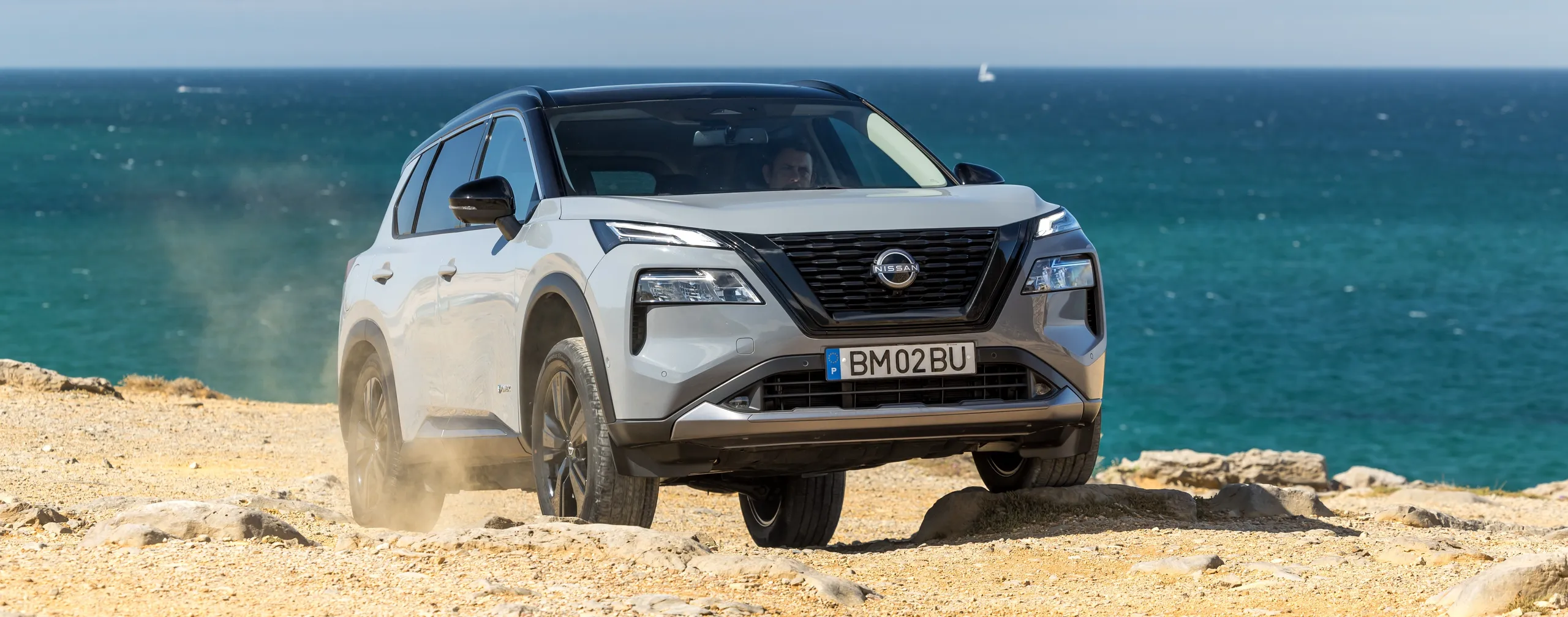 Nissan X-Trail blanco de siete plazas en terreno arenoso frente al mar