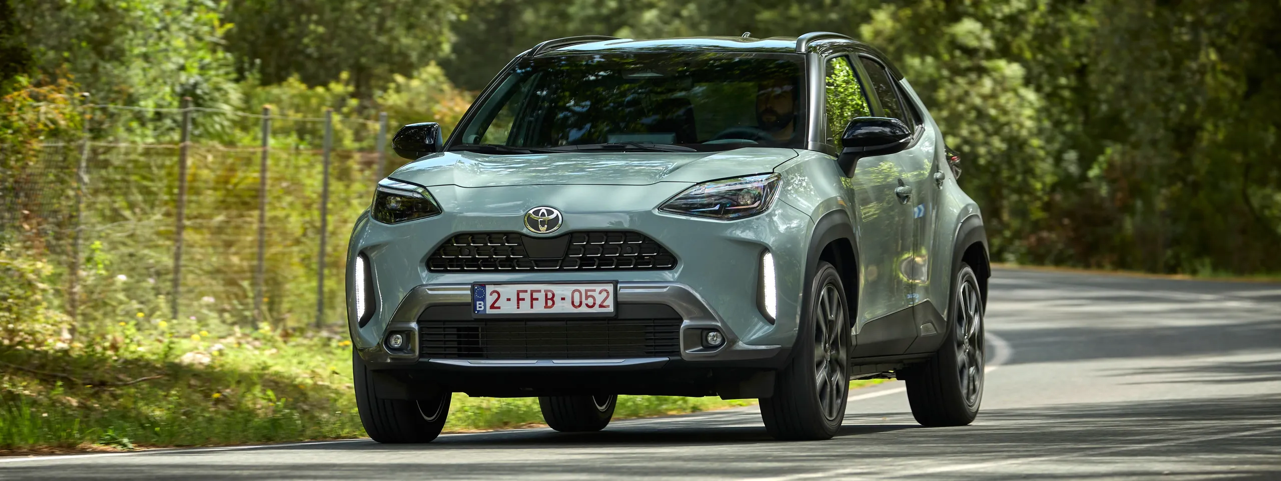 Toyota Yaris Cross gris circulando por carretera rodeada de vegetación