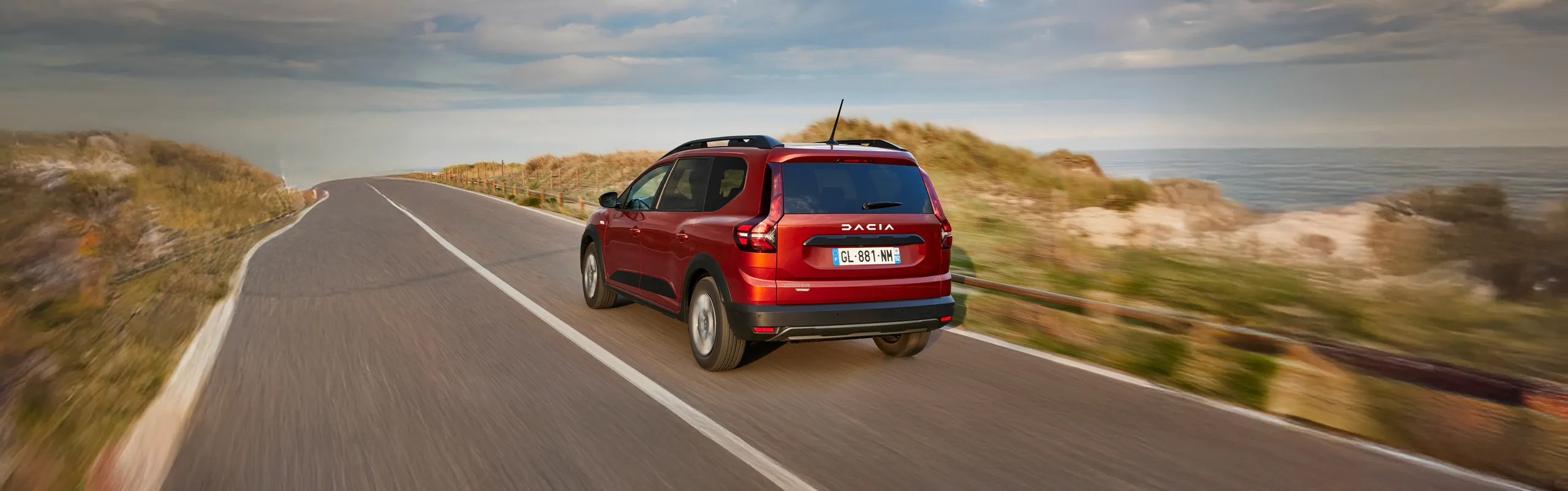 Dacia rojo circulando por carretera costera con amplio maletero para viajes