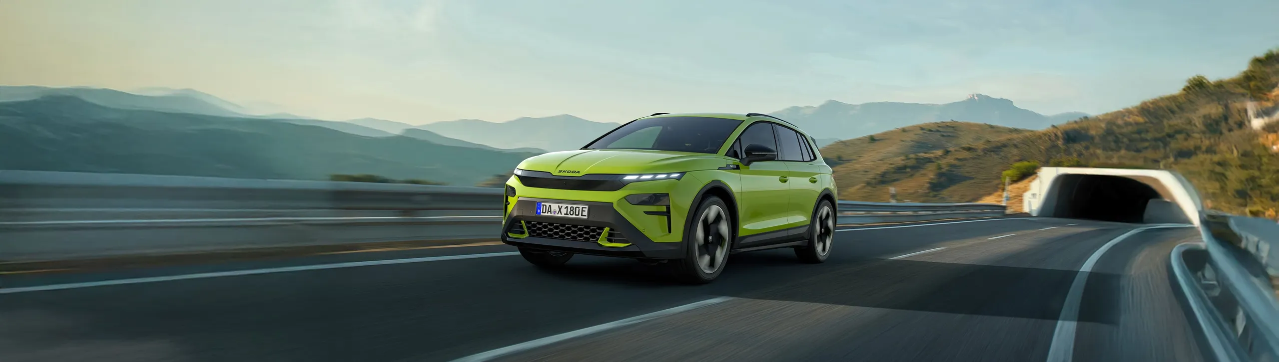 Coche eléctrico verde circulando por autopista con montañas al fondo