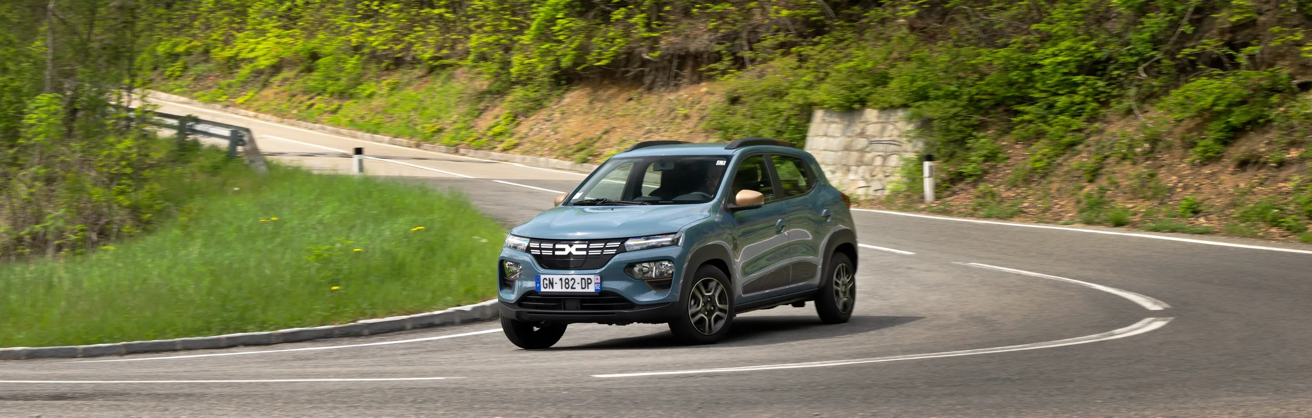 Dacia Spring eléctrico azul circulando por carretera de montaña con curva