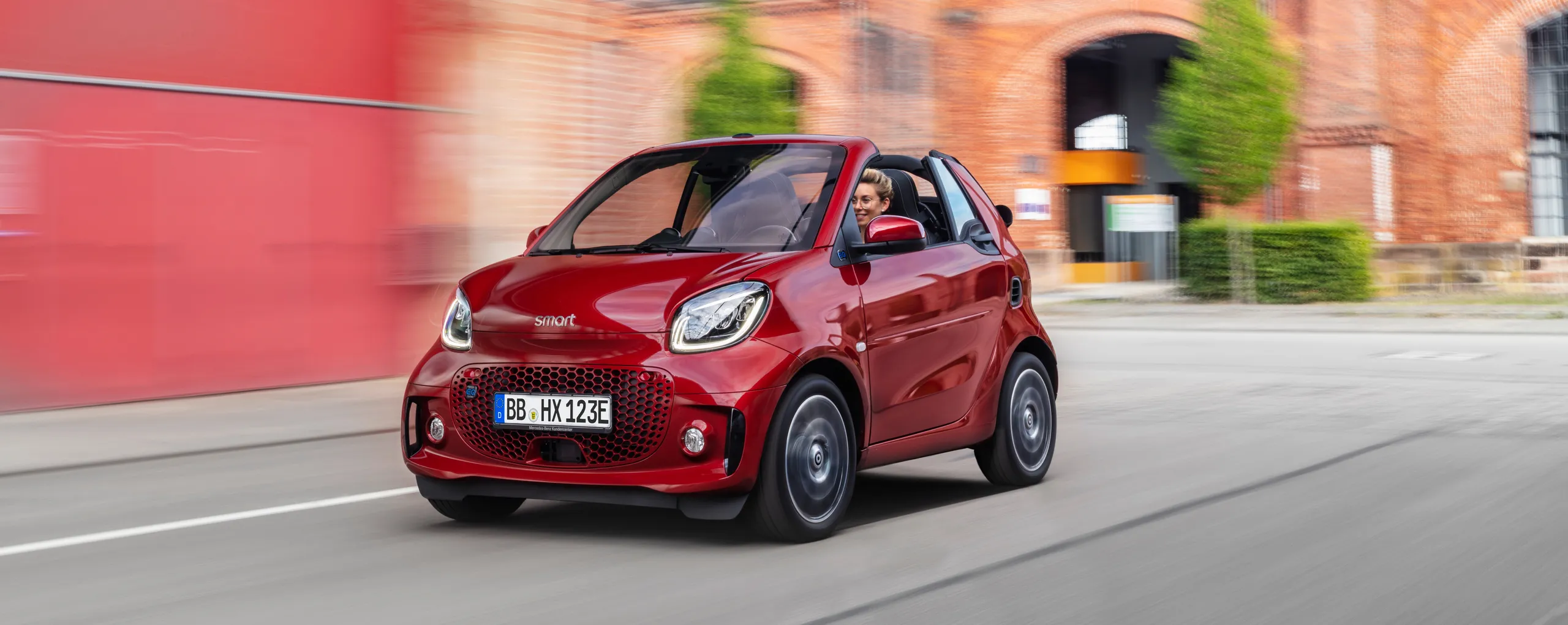 Smart forfour rojo eléctrico circulando por ciudad con edificios históricos