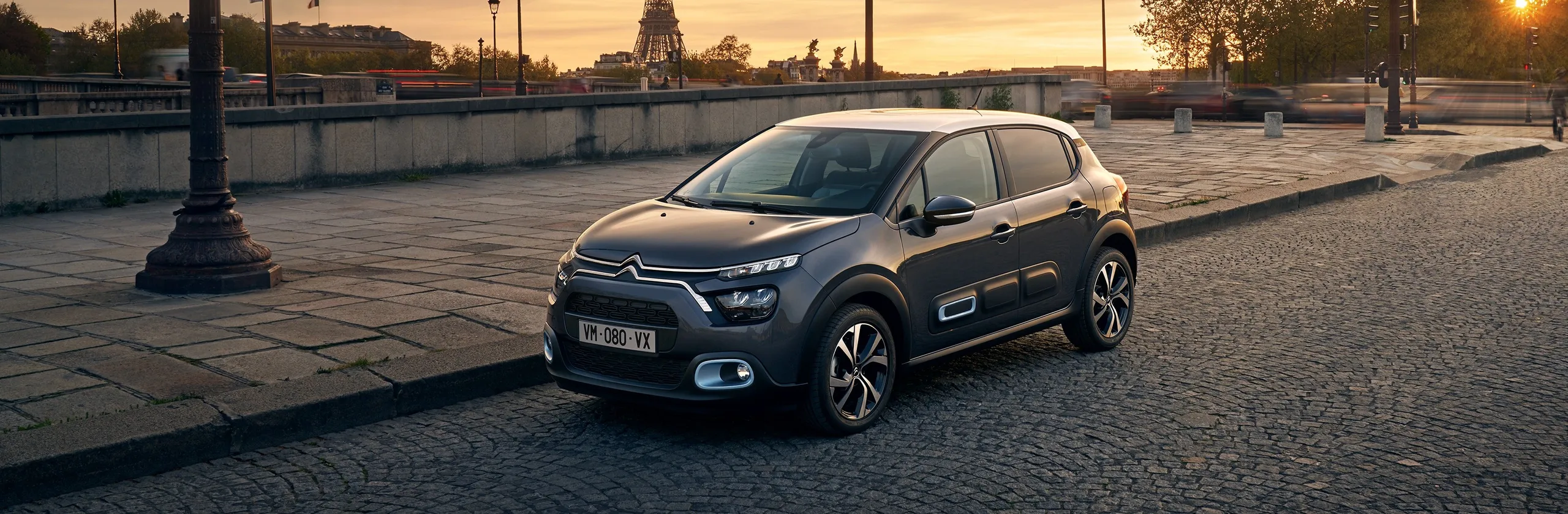 Citroën C3 gris aparcado en plaza parisina al atardecer con Torre Eiffel