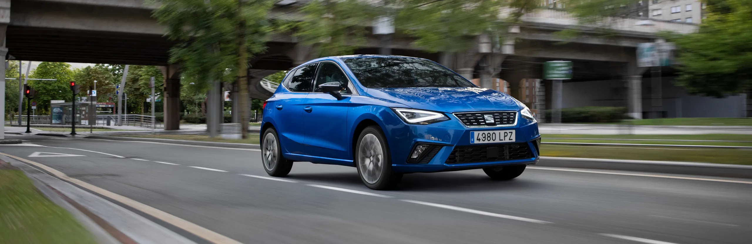 SEAT Ibiza azul circulando por una avenida urbana bajo un puente