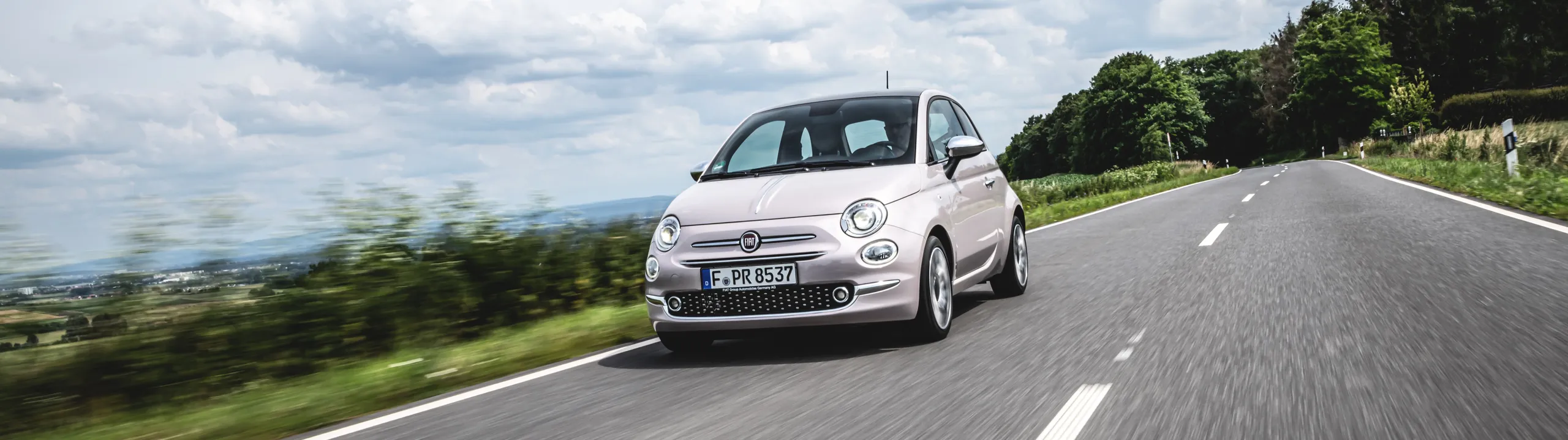 Fiat 500 blanco circulando por carretera nacional con paisaje rural