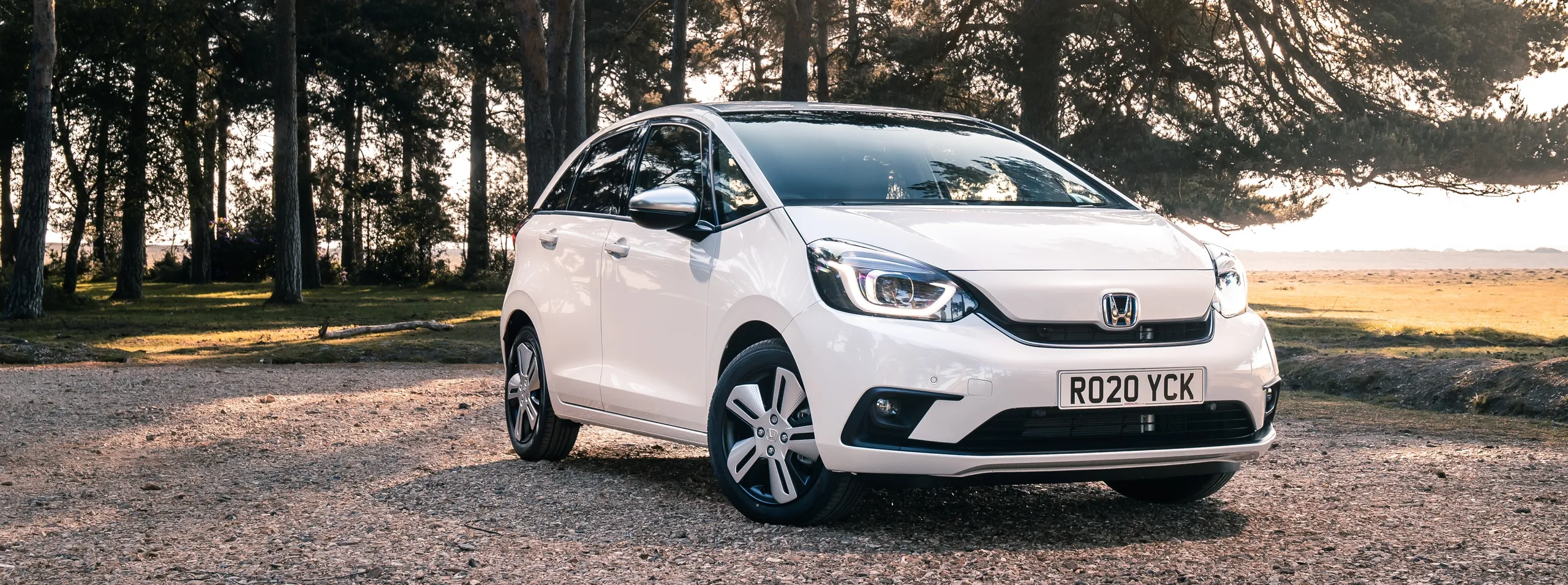 Honda Jazz e:HEV blanco en bosque, ejemplo de coche eficiente y económico