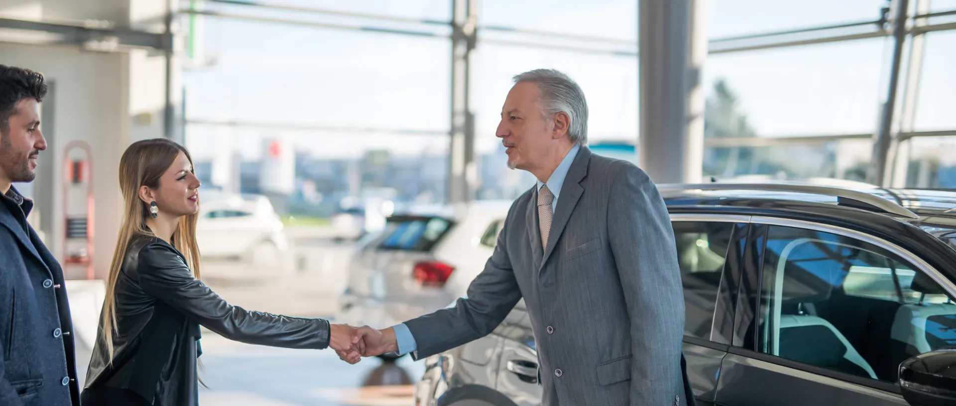 Vendedor de autos negociando venta de coche en concesionario con clientes