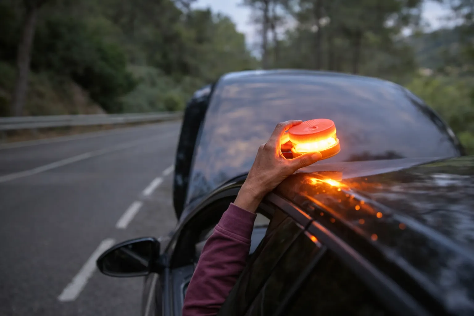 Mano sujetando baliza V16 iluminada en espejo retrovisor del coche