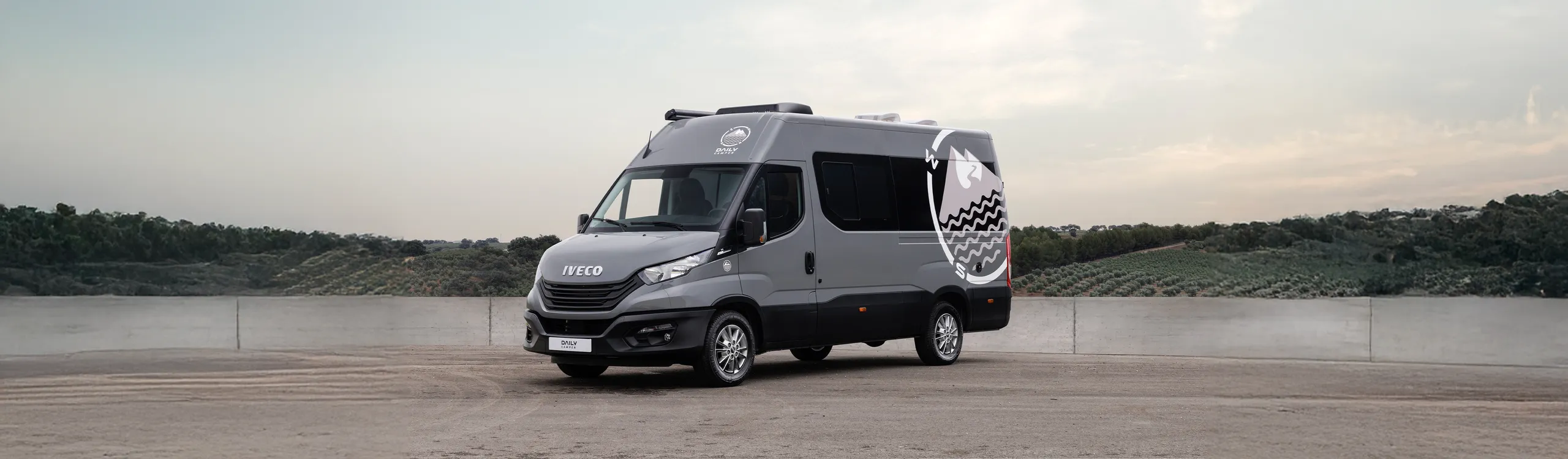Furgoneta grande IVECO Daily blanca aparcada en explanada con vistas a paisaje rural