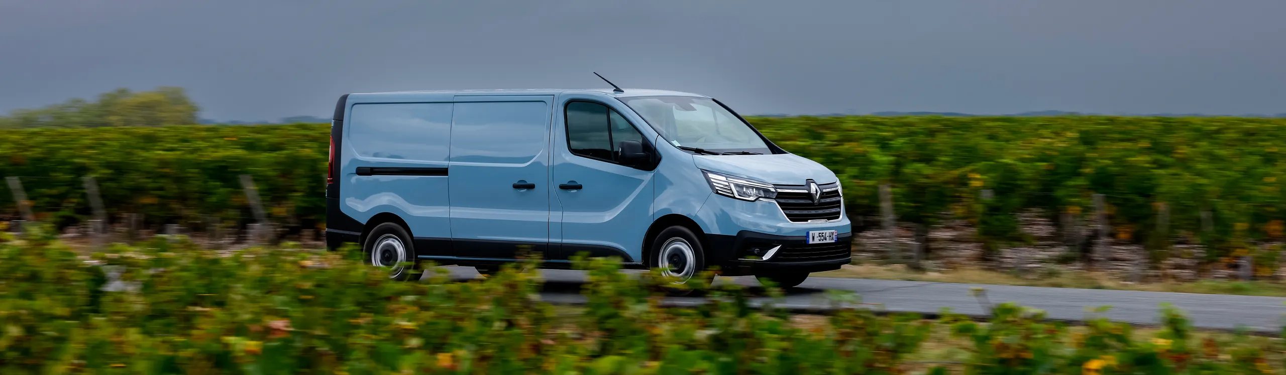 Renault Master blanca en circulación por carretera rural entre viñedos