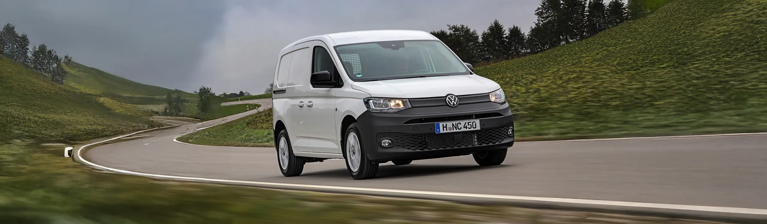 Volkswagen Caddy blanca circulando por carretera sinuosa entre montañas verdes