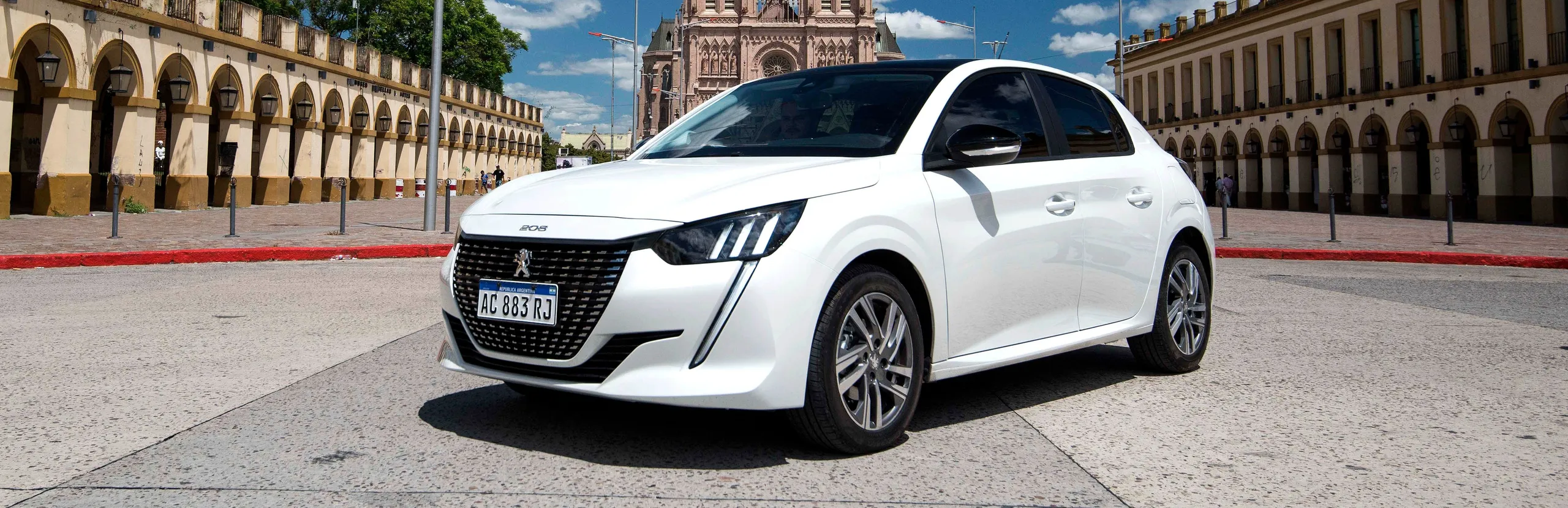 Peugeot 208 blanco aparcado en plaza histórica francesa con arquitectura clásica