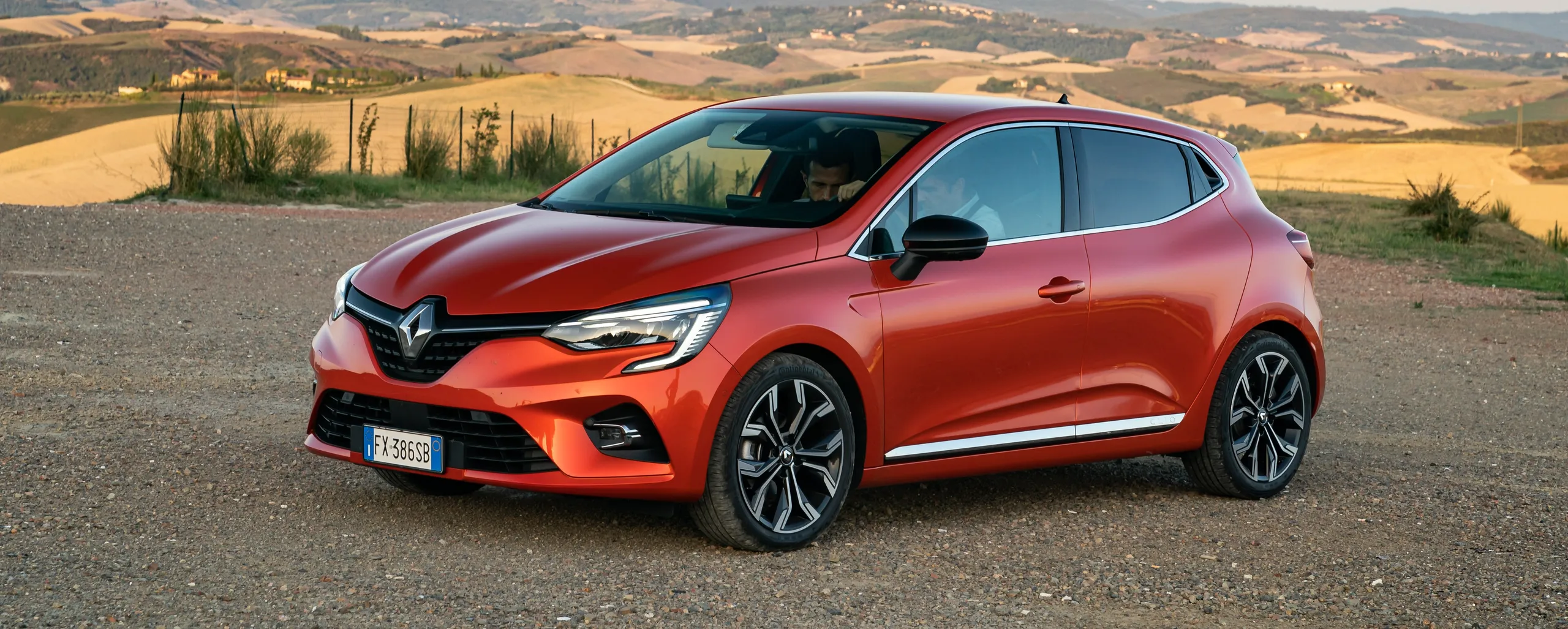 Renault Clio rojo de gasolina estacionado en carretera con paisaje rural al fondo