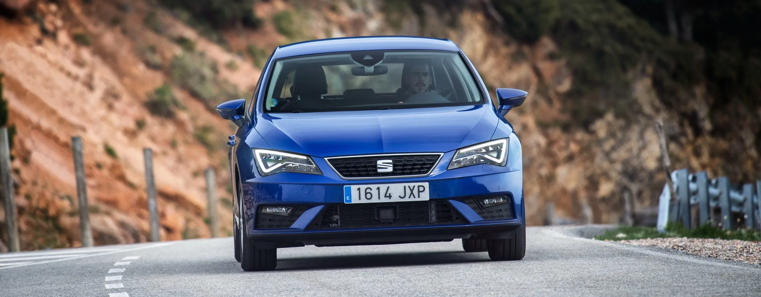 Seat León azul circulando en carretera de montaña, ejemplo de coche gasolina moderno