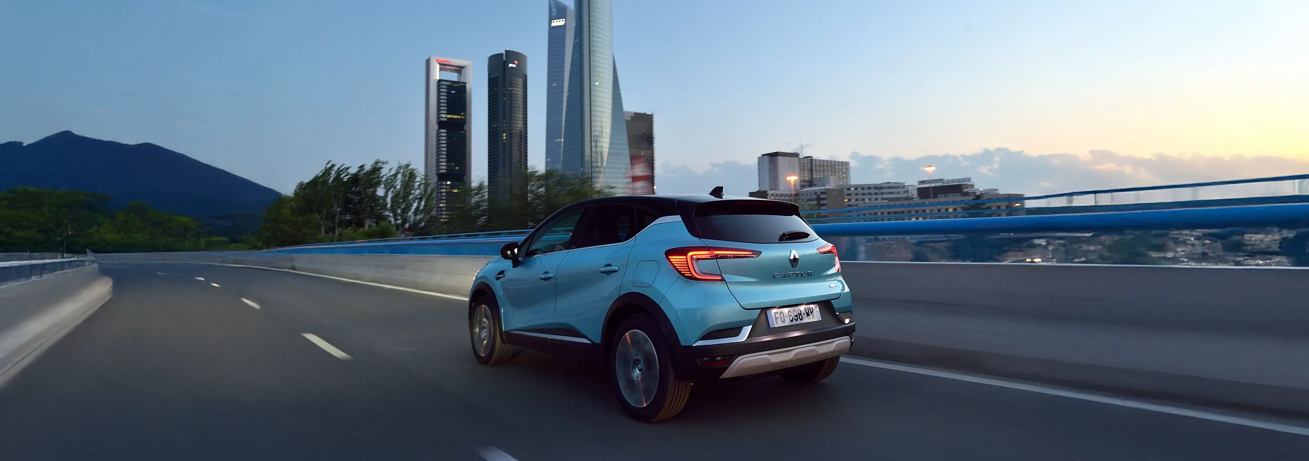 Renault Captur híbrido enchufable azul circulando por autopista con skyline urbano