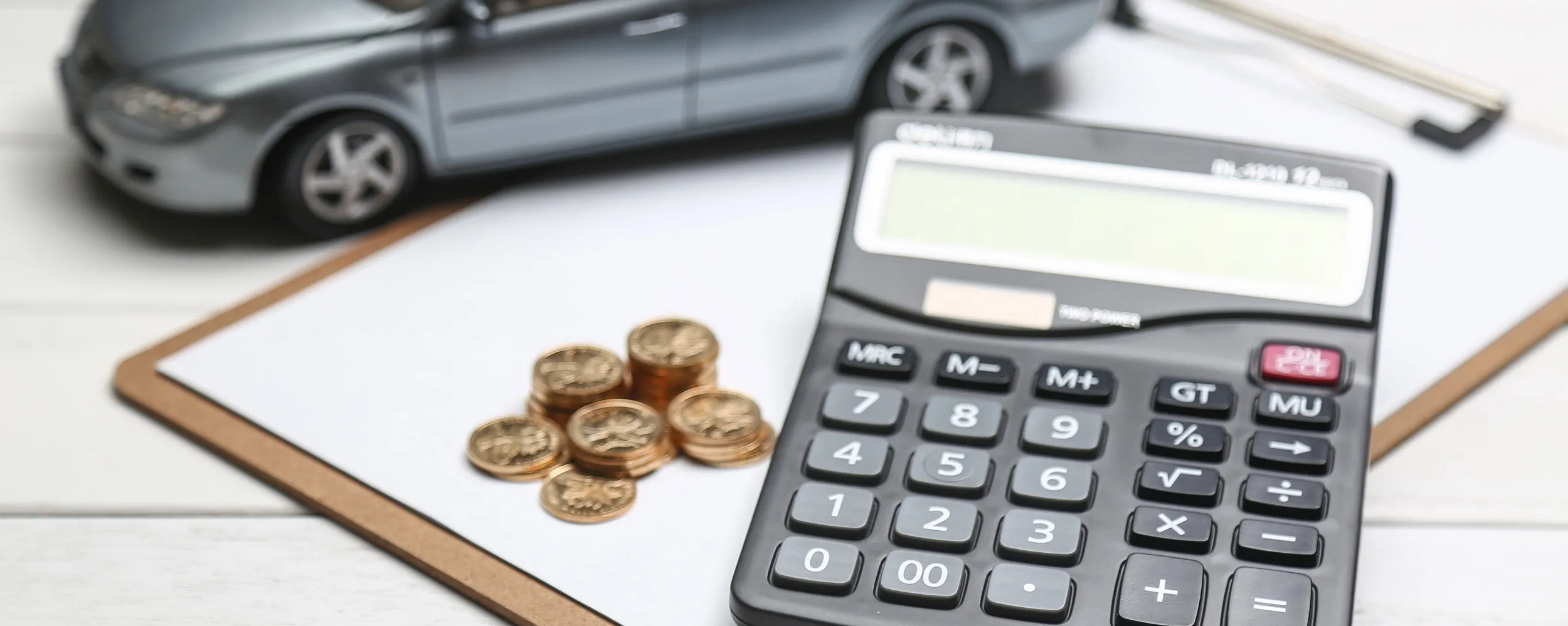 Calculadora, monedas y coche de ocasión simbolizando costes e impuestos de compra