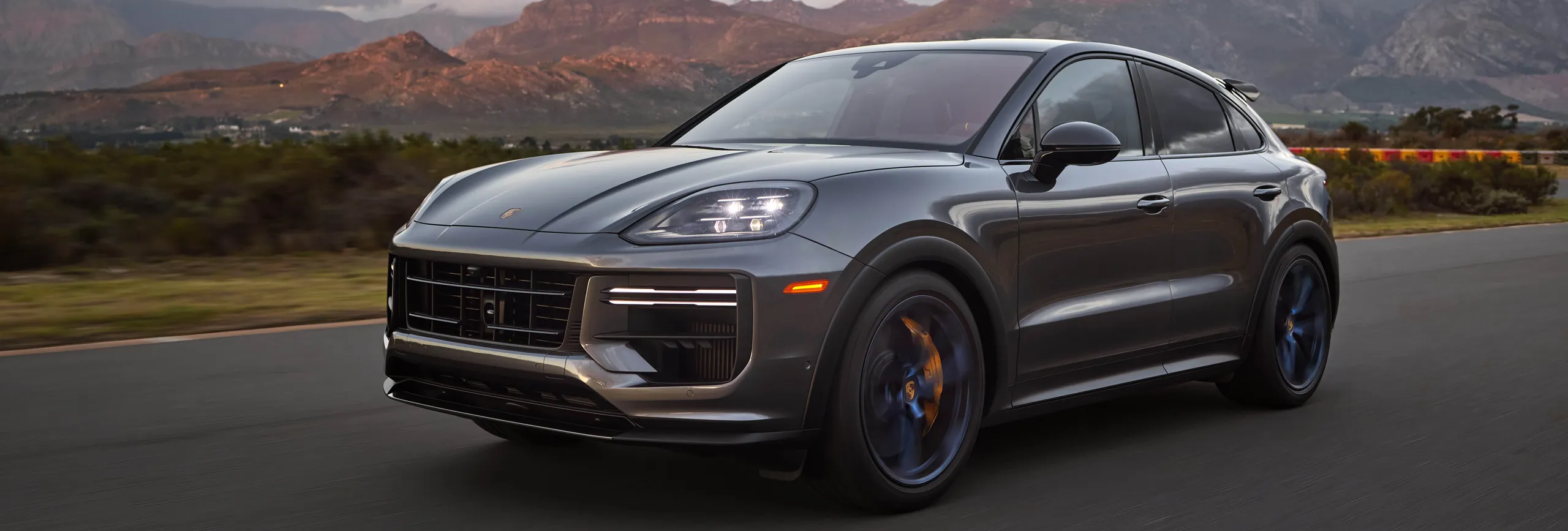 Porsche Cayenne gris oscuro en carretera con montañas al fondo
