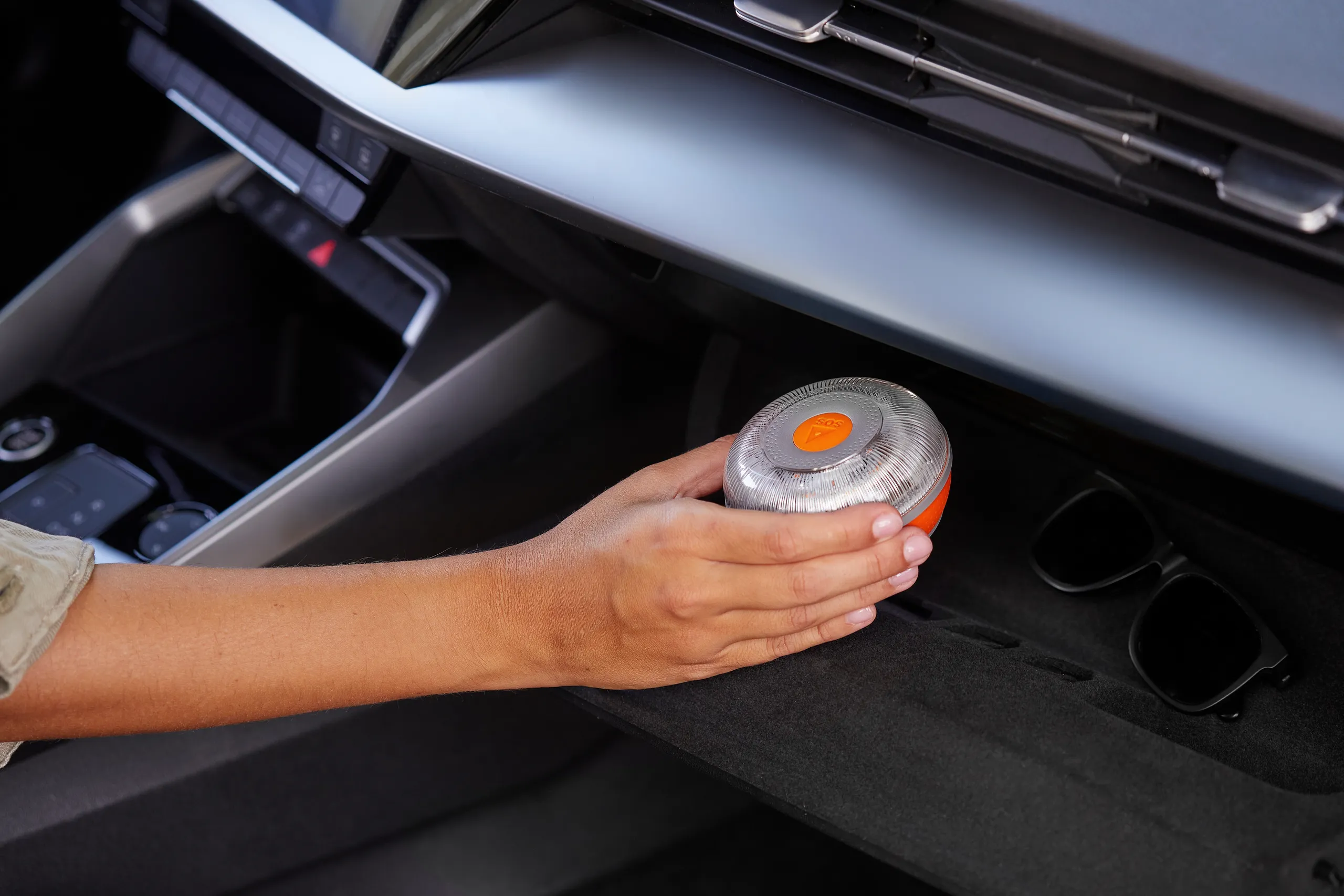 Mano sosteniendo luz de emergencia V-16 de color naranja en interior de vehículo