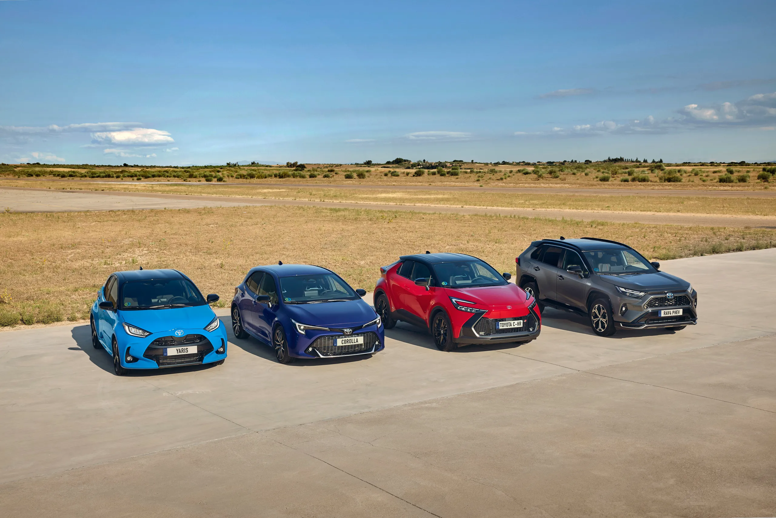 Cuatro vehículos Toyota alineados en fila sobre asfalto gris con paisaje rural
