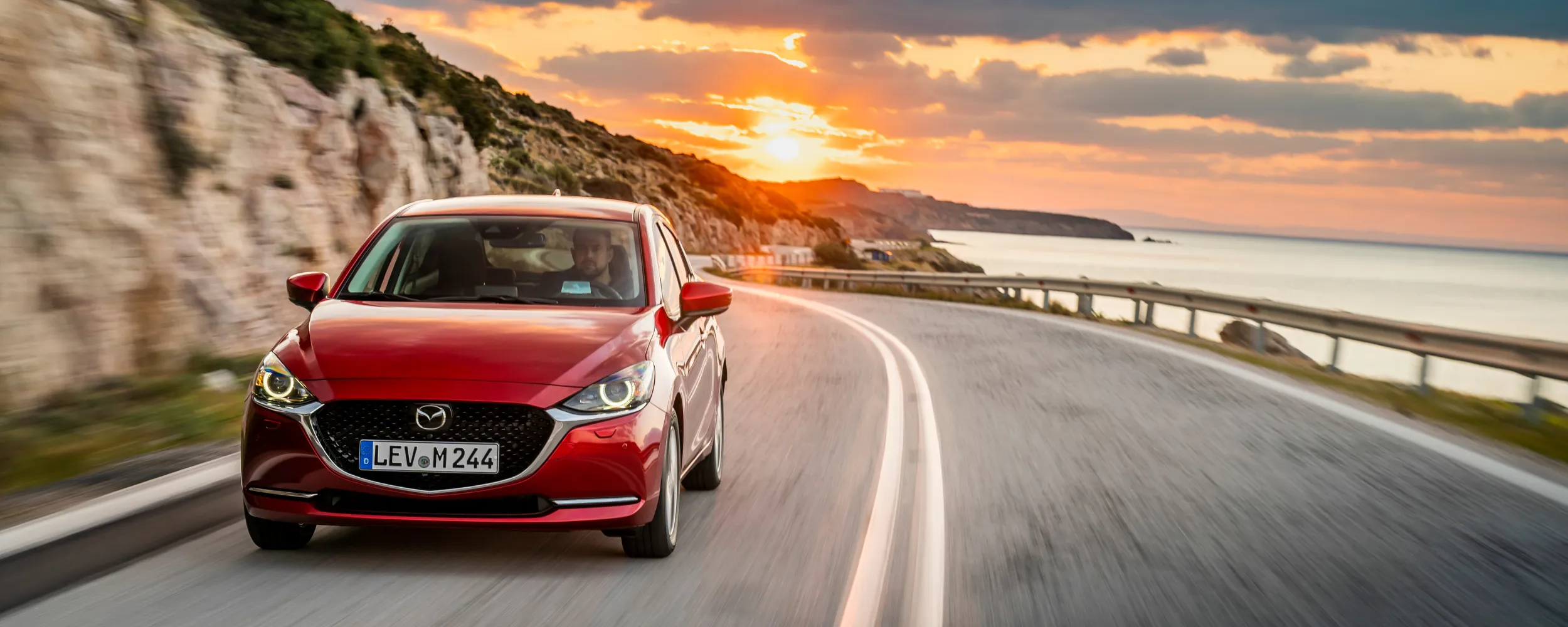 Mazda rojo circulando por carretera costera al atardecer mostrando calidad