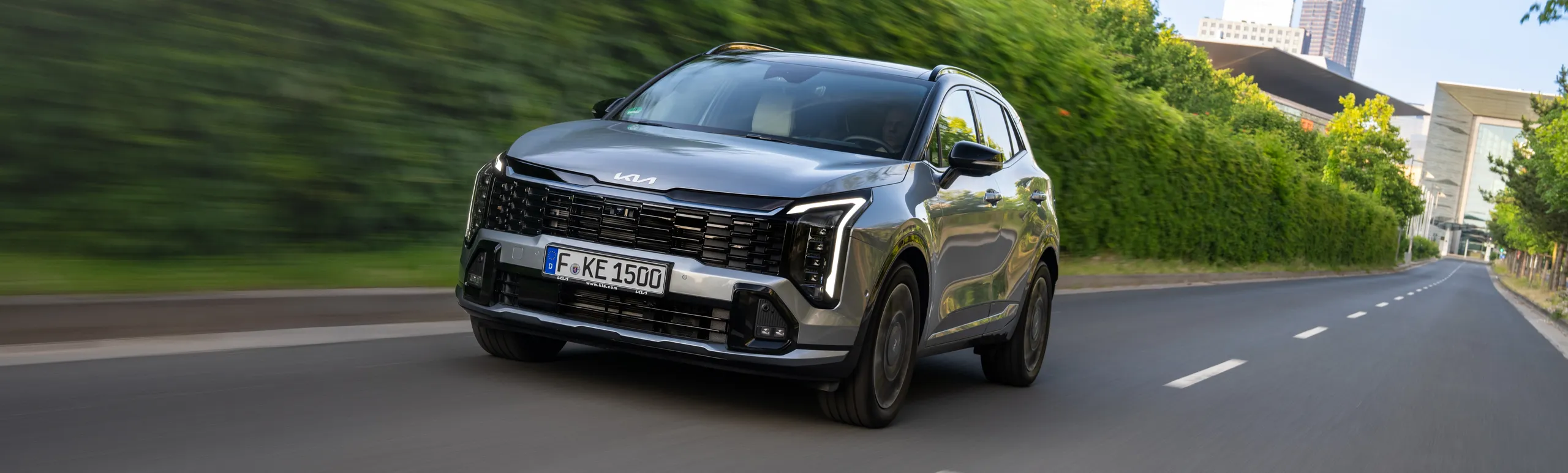 Kia Sportage gris circulando por carretera urbana con vegetación