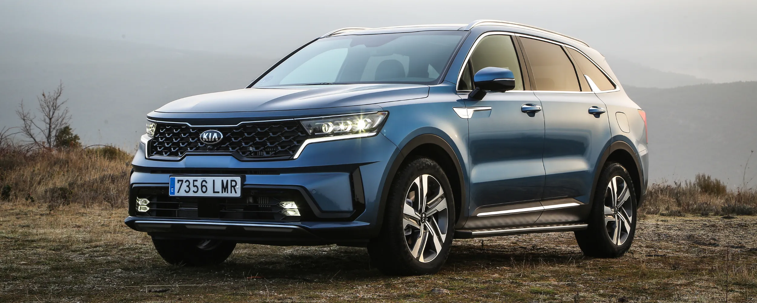 Kia Sorento SUV azul de perfil en paisaje rural con cielo nublado