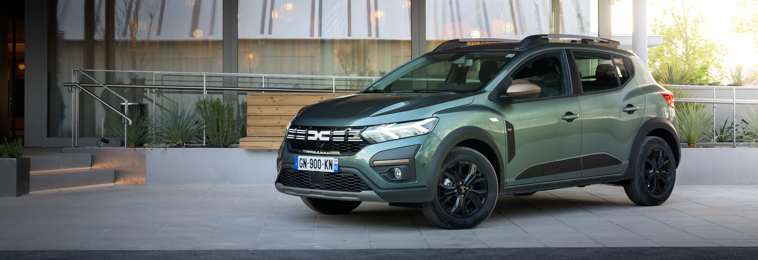 Dacia Sandero verde en aparcamiento urbano moderno con diseño práctico