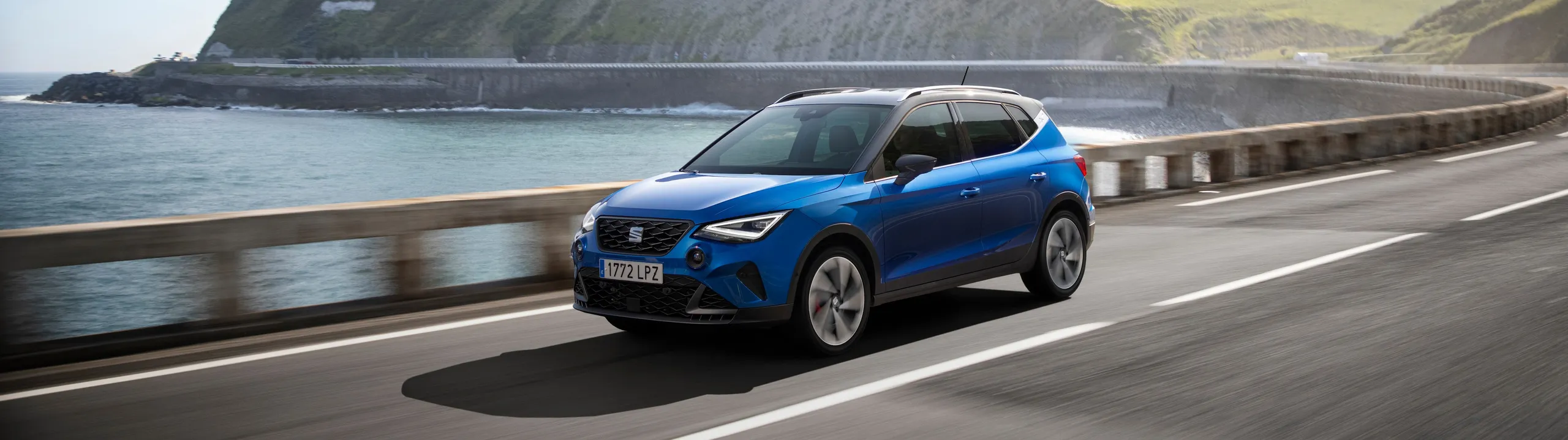 Seat Arona azul circulando por carretera costera con vistas al mar y acantilados