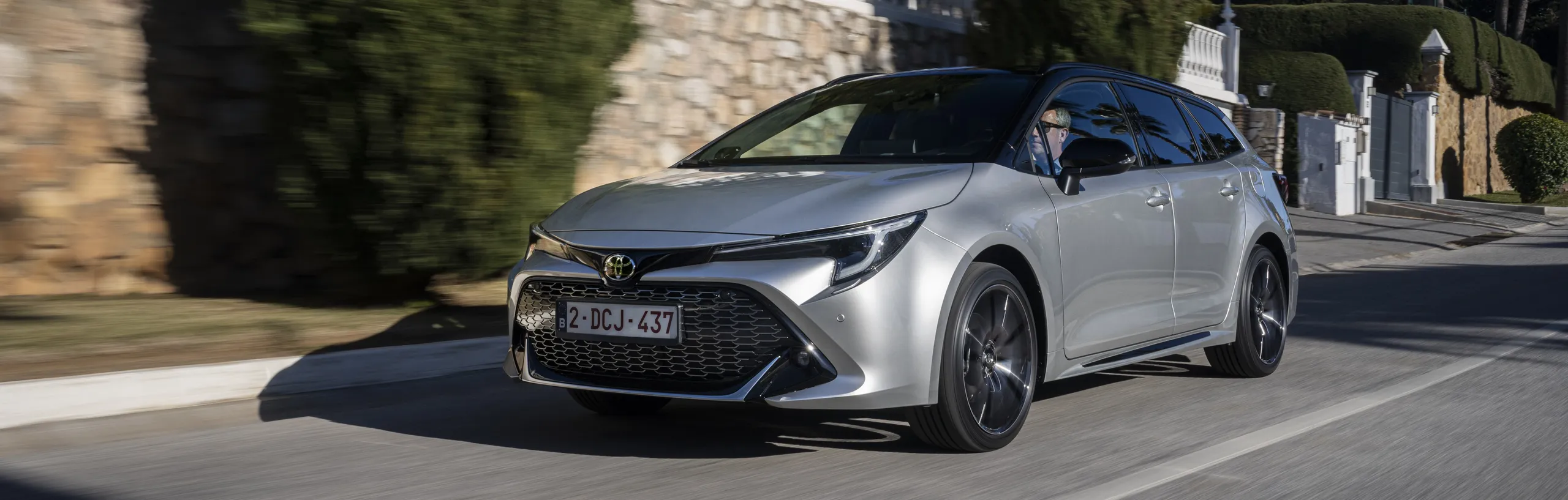 Toyota Corolla Hybrid plateado en movimiento por calle residencial con diseño moderno