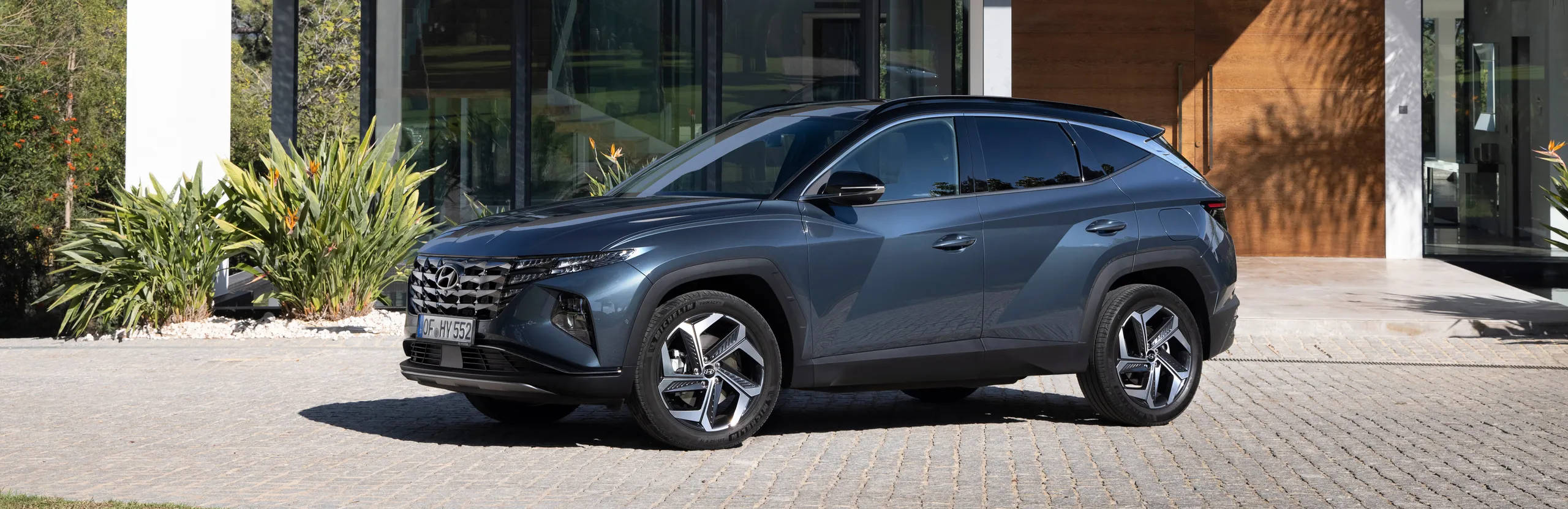 Hyundai Tucson azul oscuro aparcado en entrada de casa moderna con jardín