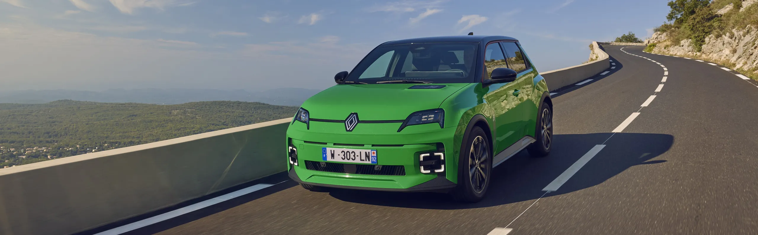 Renault 5 E-Tech verde circulando por carretera de montaña con vistas al mar