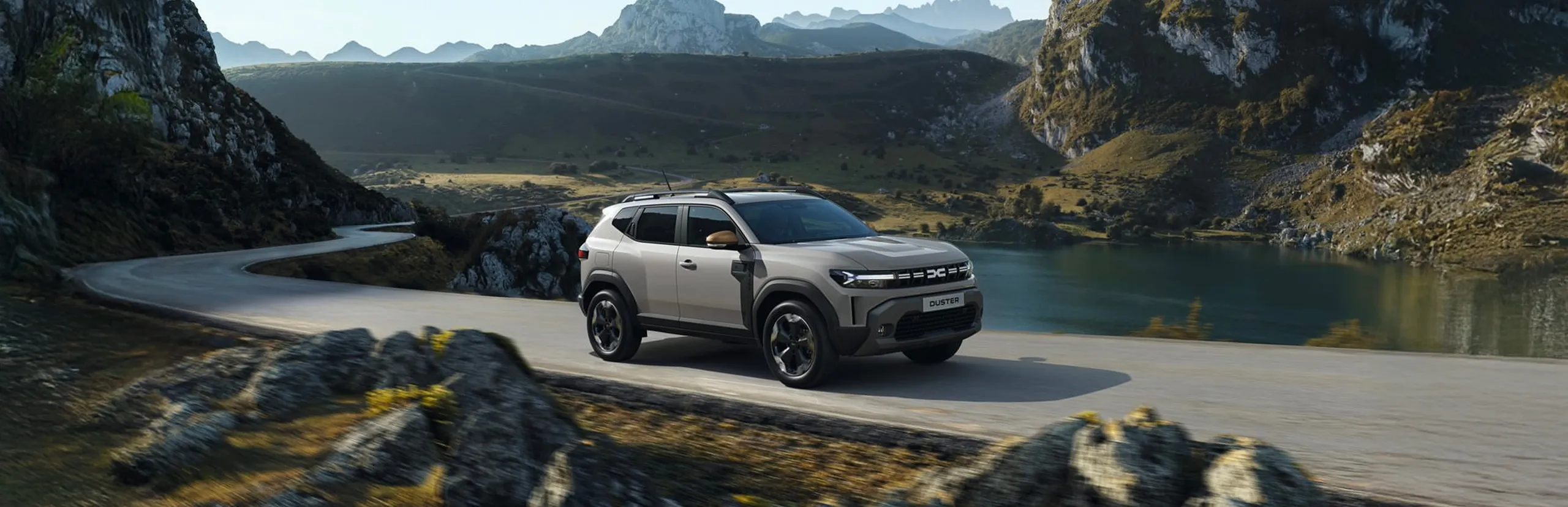 Dacia Duster eléctrico blanco en carretera de montaña con lago y acantilados