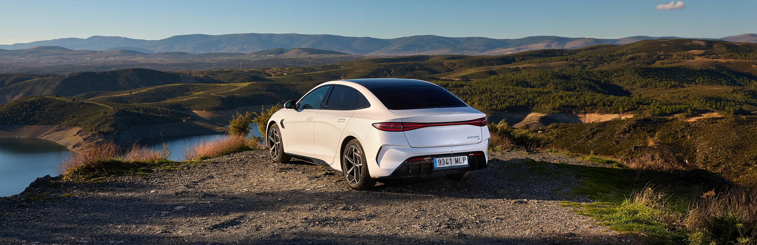 Coche eléctrico blanco aparcado en mirador con vistas a montañas y lago