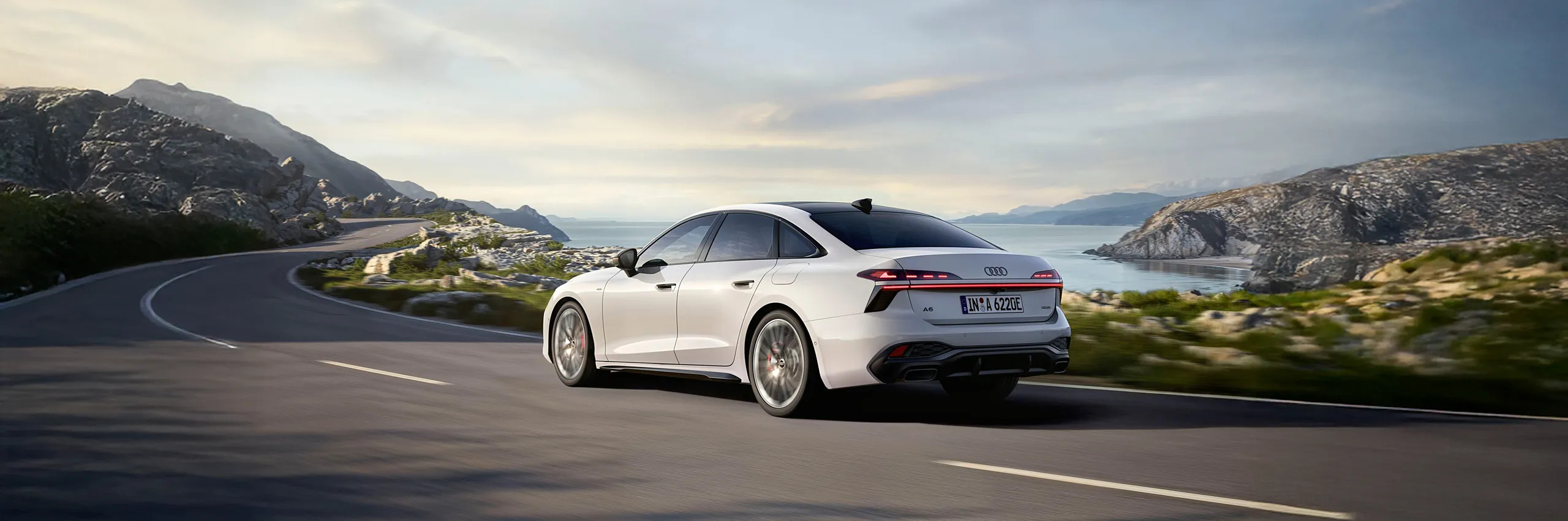 Audi A6 híbrido enchufable blanco circulando por carretera costera montañosa