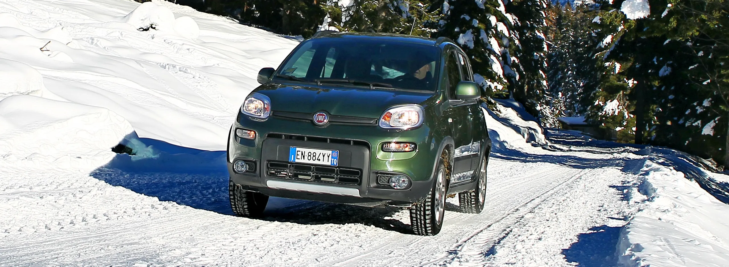 Fiat 500L verde en carretera nevada rodeado de árboles con nieve