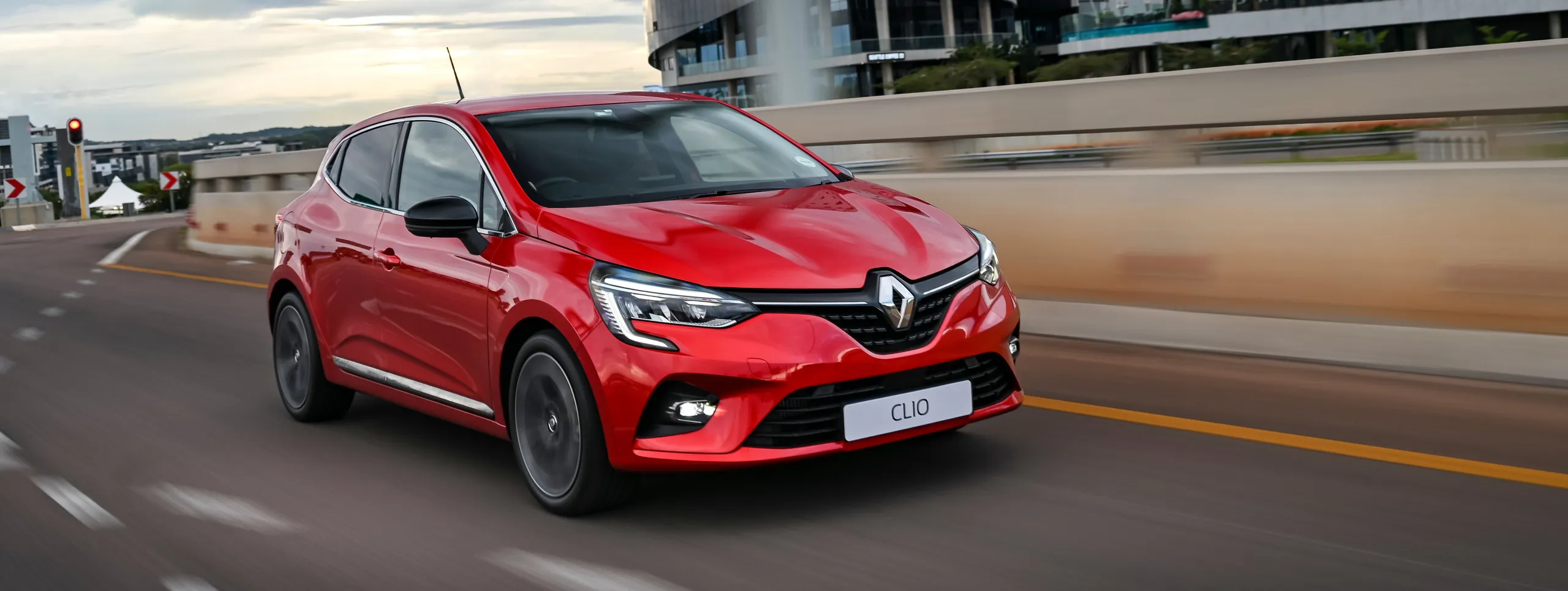 Renault Clio rojo circulando por una carretera urbana moderna