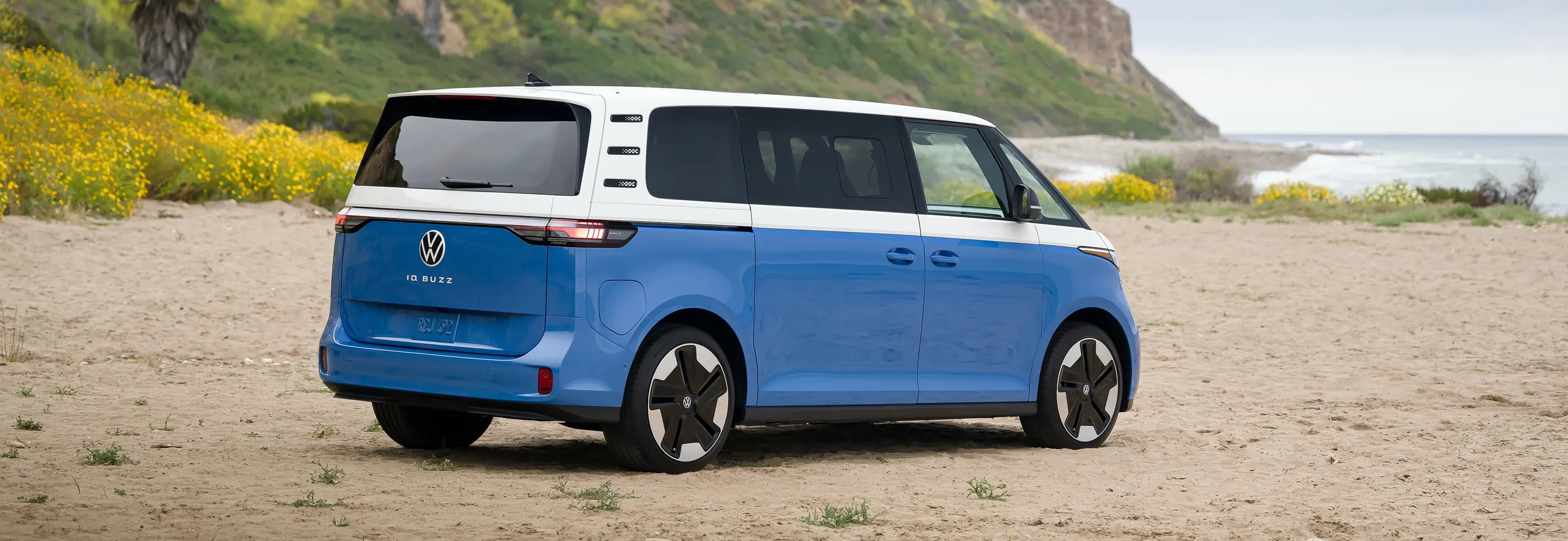 Volkswagen ID.Buzz azul y blanco en playa con acantilados verdes
