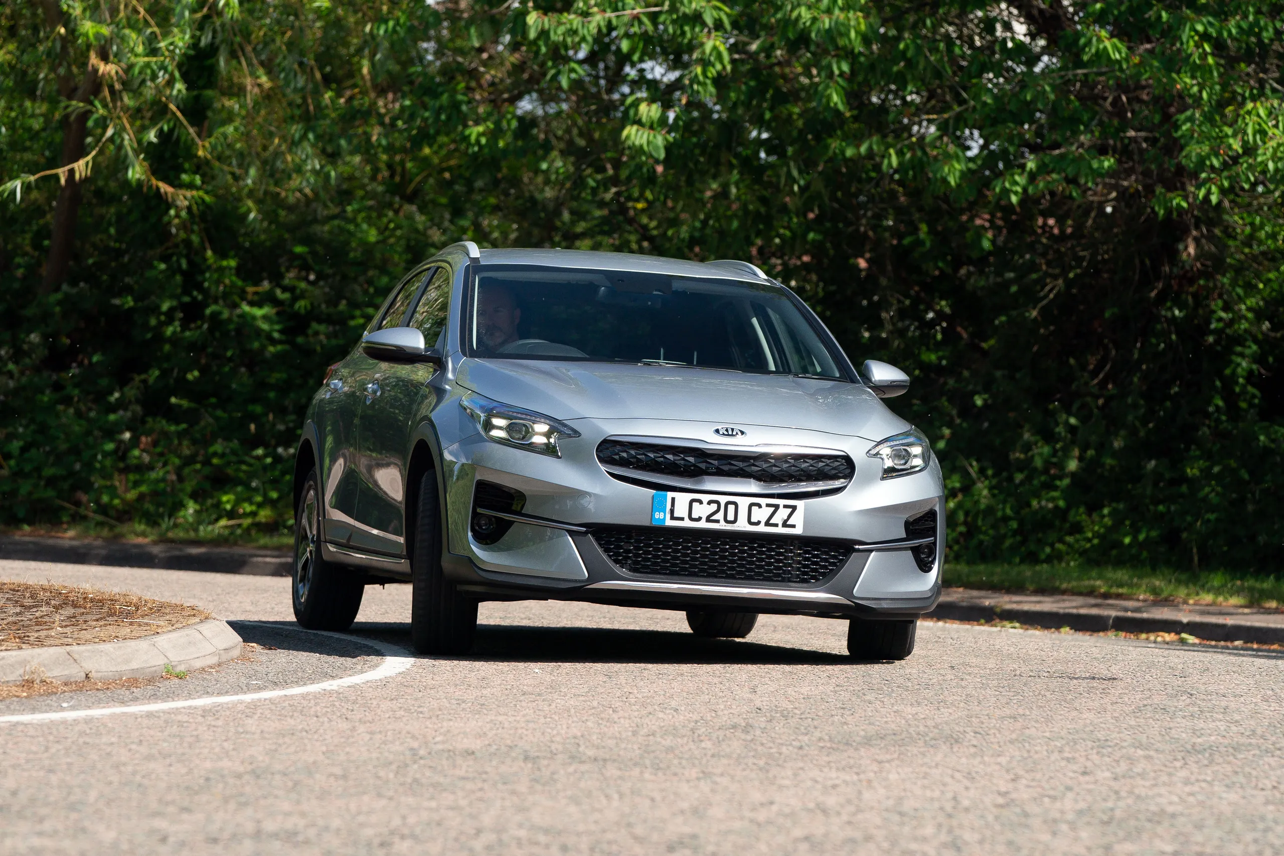 Kia XCeed híbrido enchufable plateado en carretera con vegetación