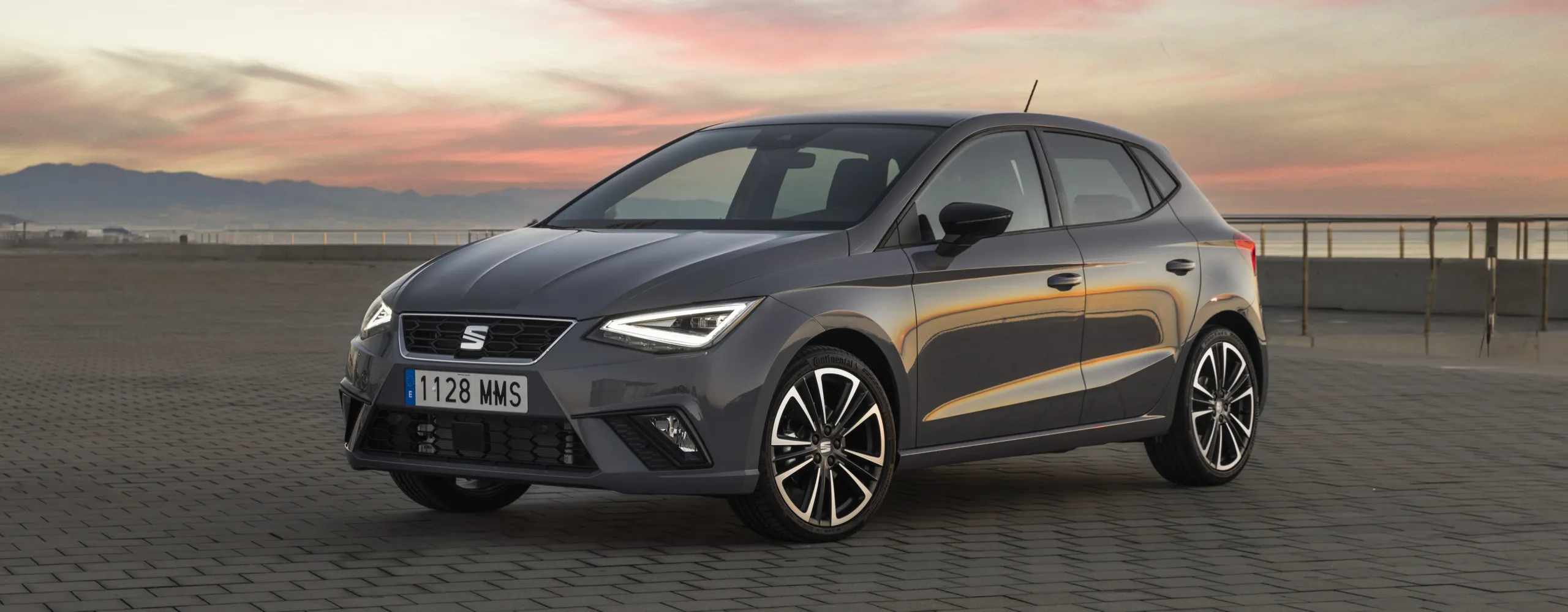 SEAT Ibiza gris con líneas naranjas aparcado en explanada al atardecer